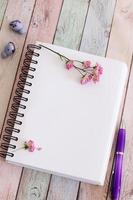 Blank notebook page with flowers and pen on wooden table photo