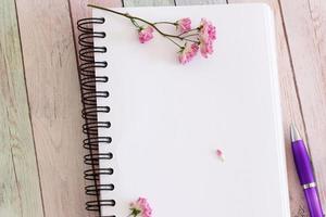 Blank notebook page with flowers and pen on wooden table photo