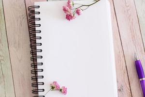 Blank notebook page with flowers and pen on wooden table photo