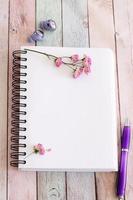 Blank notebook page with flowers and pen on wooden table photo