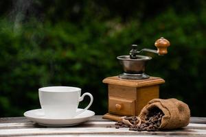 taza de café con molinillo, granos de café oscuros en el viejo piso de madera, cerca de semillas de café en un fondo natural. foto