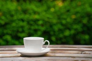 concepto de bebida de café caliente, taza de café blanco de cerámica caliente con humo en una mesa de madera antigua en un fondo natural. foto