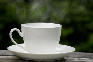 Hot Coffee Drink Concept, Hot ceramic white coffee cup with smoke on an old wooden table in a natural background. photo