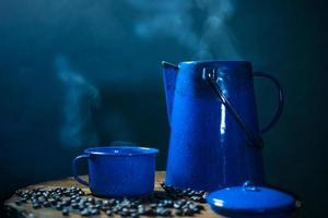 taza de café esmaltada con humo. juego de café con olla y granos de café en el viejo piso de madera foto