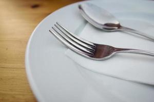 tenedor y cuchara con plato blanco sobre mesa de madera foto