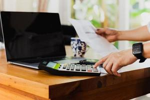 Businessman hand on calculator to calculate financial report and laptop computer on table. photo