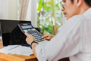 Businessman hand on calculator to calculate financial report and laptop computer on table. photo