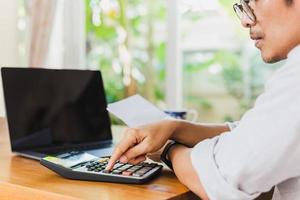 mano de hombre de negocios en la calculadora para calcular el informe financiero y la computadora portátil en la mesa.