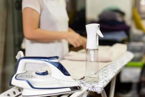 Housewife with bottle spray foggy for iron clothes on ironing board. photo