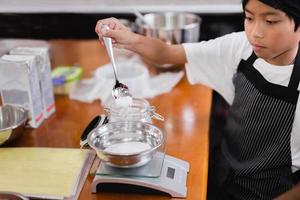 Young boy measuring ingredient for baking in kitchen. photo