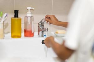 Boy rinsing toothbrush under running tap water in bathroom sink. photo