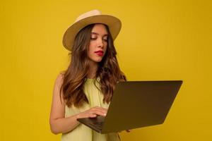 Close-up portrait of european stylish girl wearing hat with long wavy hair using laptop over isolated background photo