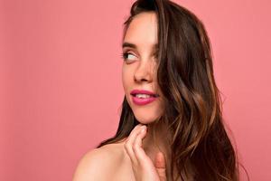 Close up studio portrait of european woman with perfect skin, adorable smile and nude make up posing over pink background photo