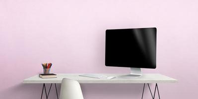 Blank computer display on work desk with pens and book beside. Pink wall in background photo