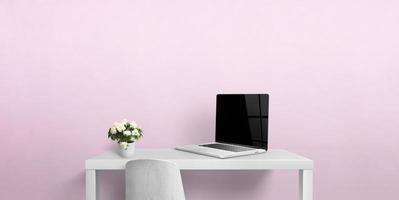 pequeño escritorio de trabajo con ordenador portátil y flores. pantalla de portátil en blanco para la presentación de la página web. copie el espacio en la pared rosa foto