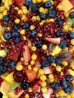 A closeup photo of a fruit salad containing fruit including strawberries, blueberries, pomegranate, grapes, sweet melon and gooseberries that looks very tasty