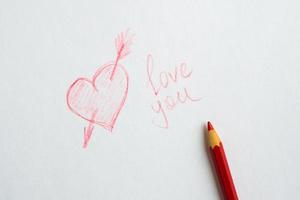 Heart drawn on paper, the inscription love you and a red pencil on white paper. photo