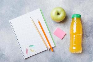 School supplies and Breakfast crackers, orange juice and fresh Apple on the grey table with copy space. concept school. photo