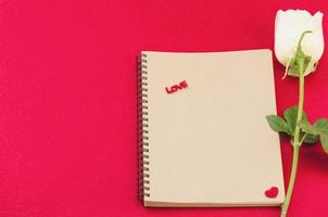 rosa blanca con cuaderno sobre fondo rojo - concepto de tarjeta electrónica de amor y flor foto