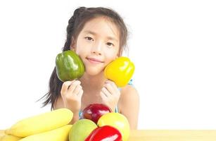 Gril asiático saludable mostrando expresión feliz con variedad de frutas y verduras de colores sobre fondo blanco. foto