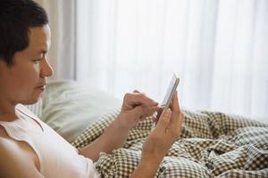 Man using mobile phone while wake up on bed in the morning - technology in every day life concept photo