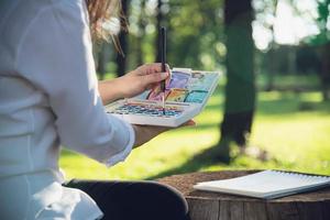 relájese mujer pintando obras de arte de color de agua en la naturaleza verde del bosque del jardín - personas con arte creativo en la naturaleza reducción del estrés y concepto de meditación foto