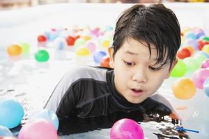 niño jugando con una pelota de colores en un pequeño juguete de piscina - niño feliz en el concepto de juguete de piscina de agua foto