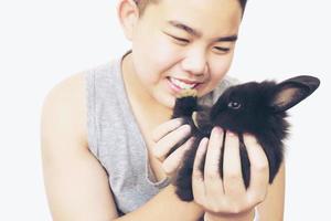 niño asiático jugando con un encantador conejo bebé aislado sobre blanco foto