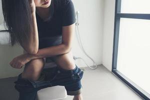 Woman sitting on toilet bowl holding tissue paper  - health problem concept photo