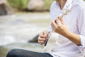 Man play ukulele new to the river- people and music instrument life style in nature concept photo