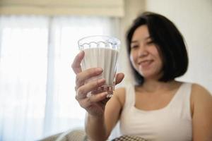 Asian woman drink milk after wake up in the morning sitting on a bed - health care concept photo