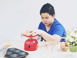 A boy is weighing raw eggs preparing to make a cake. photo