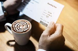 hombre que sostiene la taza de café y la tarjeta de embarque esperando el vuelo en avión para el trabajo de negocios foto