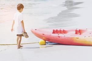 Kid walking and looking at canoe on beach photo