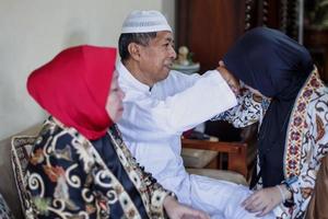 Portrait of young muslim woman kneeling and kiss her parent's hand asking for forgivness. Indonesian traditional gesture called sungkem. Eid mubarak, ramadan, idul fitri day concept. photo