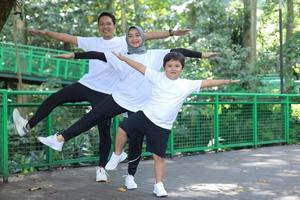 madre y padre asiáticos jóvenes practicando yoga y equilibrando el cuerpo junto con su hijo en el parque verde. deporte de diversión familiar. foto