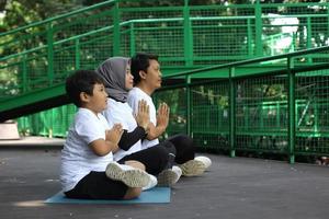 Young Asian family meditating yoga pose together in namaste hands at the greenery park. Healthy lifestyle family concept. photo
