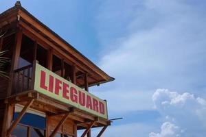 Wooden tower with lifeguard sign on the beach under the blue sky photo