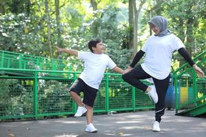 Asian muslim mom and son hold hands while balancing body, exercising and spend time together in green park. photo