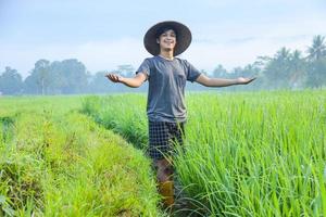 Attractive cheerful young Asian farmer standing, smiling and spreading arms showing success to growing paddy rice in the rice field. Modern agriculture concept. photo