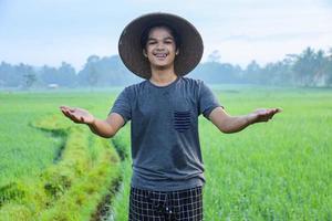 Attractive cheerful young Asian farmer standing, smiling and spreading arms showing success to growing paddy rice in the rice field. Modern agriculture concept. photo