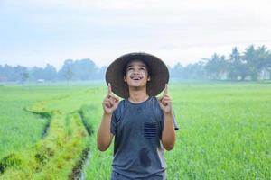 retrato de un joven granjero asiático alegre y atractivo de pie y mostrando un momento aha teniendo idea del campo de arroz. concepto de agricultura moderna. foto