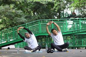 joven pareja musulmana asiática estirándose juntos en una alfombra de yoga en el parque verde foto