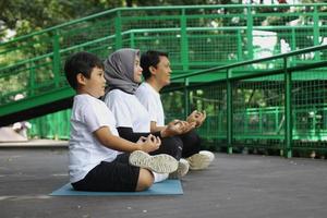 Young Asian family doing exercise in meditate yoga pose together at the greenery park. Healthy lifestyle family concept. photo