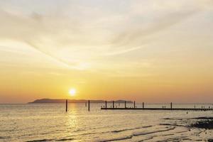 Landscape of colorful sunset shining over bright orange waters of the ocean. Silhouette of tourists walking, relaxing and taking photos sundown on beach of tropical sunset at Koh Larn Beach.