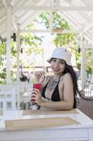 joven hermosa y sexy mujer en bikini con jugo fresco en el restaurante, sonriendo con felicidad de vacaciones en verano. chica muy sonriente bebiendo un sabroso cóctel rojo dulce, increíble día relajante foto