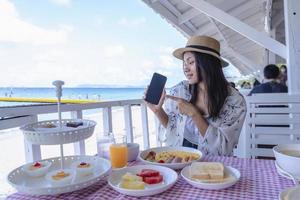 Traveler girl showing smartphone blank screen advertising application to shopping and paid online by mobile app. Young Asia lady show empty smartphone screen with a positive expression. photo