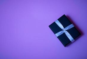 Small rectangular black gift box on a purple background, top view photo