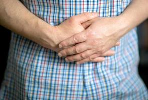 A man in a shirt keeps his hands on his stomach, close-up on his hands photo