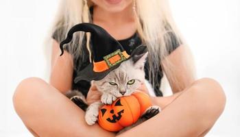 Disgruntled cat in the halloween costume with toy pumpkin in the arms of a girl photo